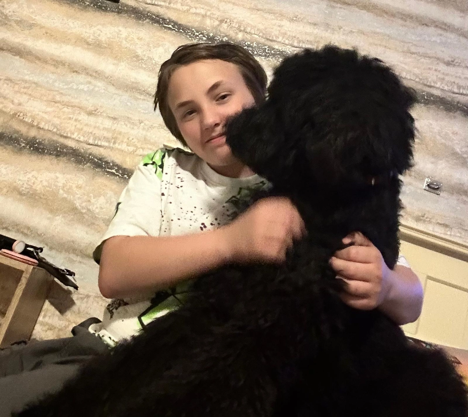 Allerbienen Celle - Betreuungsdienst - Ein lächelndes Kind umarmt draußen einen großen, flauschigen schwarzen Hund.